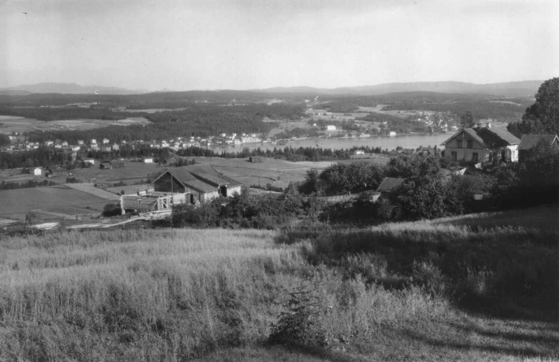 Nore, Uvdal 1930. Oversiktsbilde. Landskap med gårder. i forgrunnen. Numedalslågen med bebyggelse og skogkledde åser i bakgrunnen.