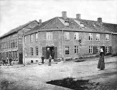 FOLK FORAN JØNSRUDGÅRDEN VED STORTORGET i Hamar, TORGGATA - KIRKEGATA, JOHN KRISTIANSENS SPISE, KAFE, THE M. M. INDSKJÆNKING AF ØL & VIN, ALKOHOL. 
Gården ble satt opp i 1852 og revet i 1962. Her holdt den store industriutstillingen for Hamar i 1880 holdt til. . Foto/Photo.
