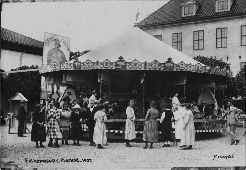 Postkort. Marked på Norsk Folkemuseum i 1922. Karusell på museets torg. Skilt med påskriften "Kjæmpekvinden".