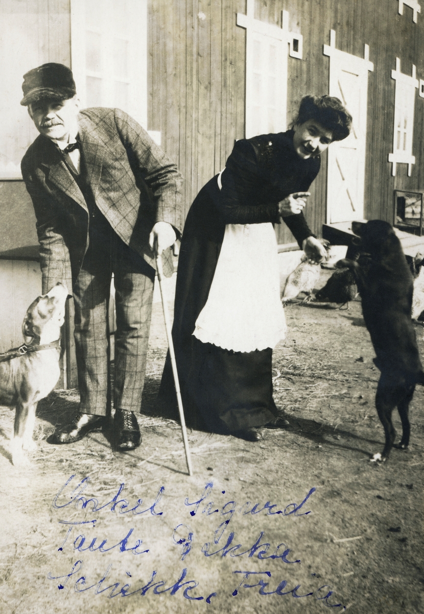Ekteparet Sigurd Svenneby (1879-1965) og Fredrikke Svenneby, f. Fossum (1880-1952), fotografert med hver sin hund framfor låvebygningen på Langbakken i Våler i Solør, der ekteparet bodde fra 1909 til 1921. Han vart kledd i en rutete dress med vest og kvit skjorte under, og på hodet hadde han ei skyggelue. Han støttet seg på en spaserstokk. Hun var iført en lang, mørk kjole med kvitt forkle. Sigurd Svenneby var født på en av storgardene i Våler og utdannet jurist. Med denne faglige ballasten flyttet han tilbake til hjembygda hvor han ved siden av sakførerpraksisen opptrådte som tømmerbetinger og skogspekulant. Det var økonomien i disse aktivitetene som gjorde det mulig for ham å bygge et herskapshjem for seg sjøl og kona på Langbakken, og det var krakket i skognæringene om lag 12 år seinere som gjorde at de måtte forlate det påkostete hjemmet sitt. Låvebygningen i bakgrunnen ble oppført i 1907.