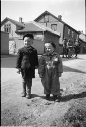 To ukjente barn langs Storgata i Moelv, veikrysset ved hotellet og sparebanken foran en gruppe hus. 